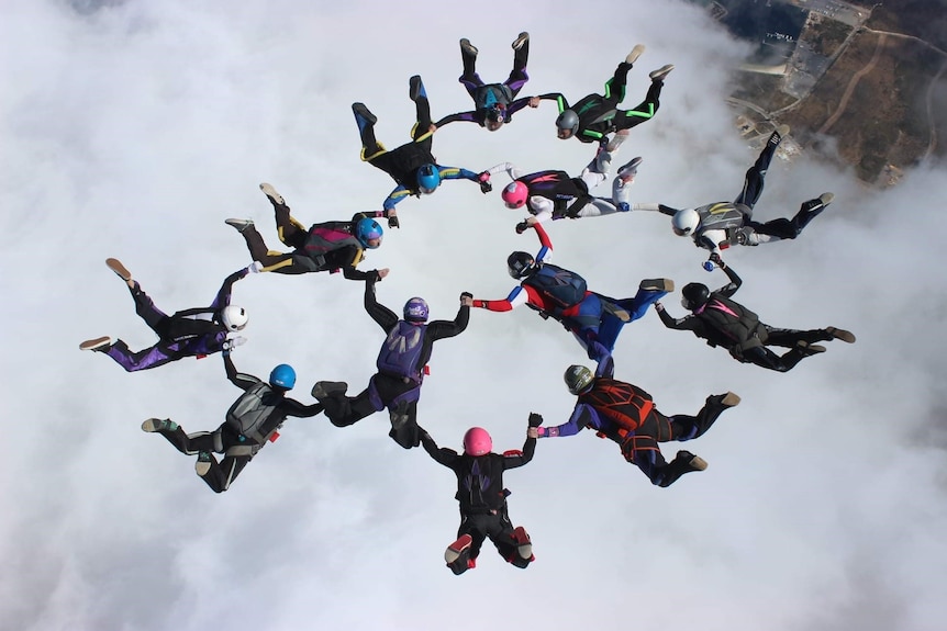 A group of skydivers form a circle while hovering above a cloud.