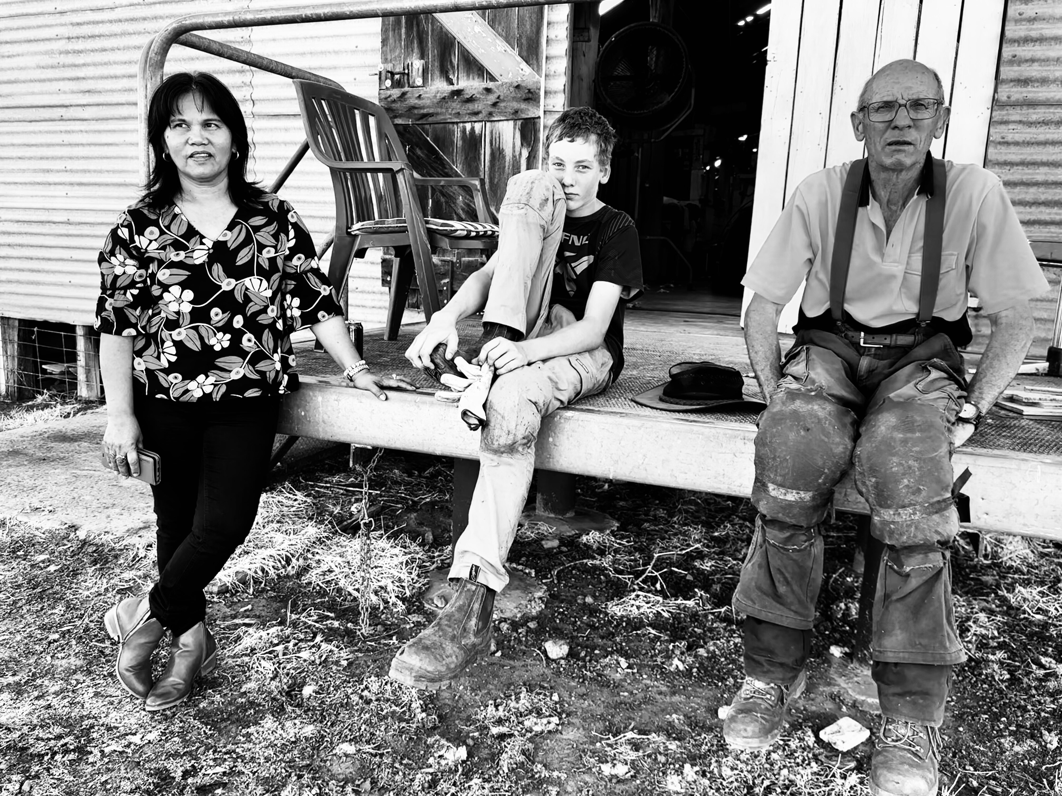 a woman, teenager and man sit outside a woolshed
