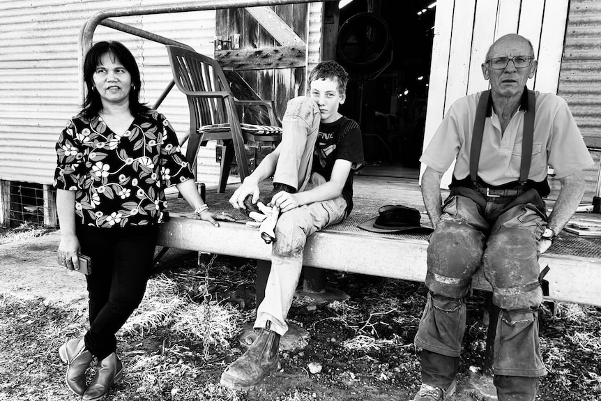 a woman, teenager and man sit outside a woolshed