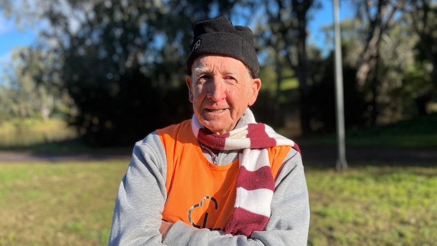 A man in a beanie, scarf, jumper and fluoro vest smiles at the camera