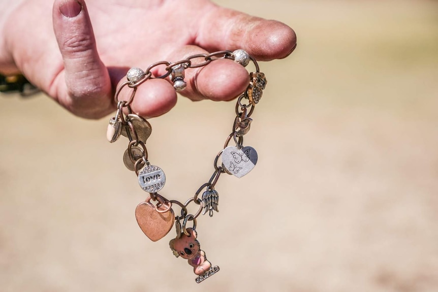 A man's hand holding a charm bracelet.