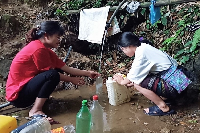 Two girls holding empty bottles over a stream of muddy water in Vietnam.