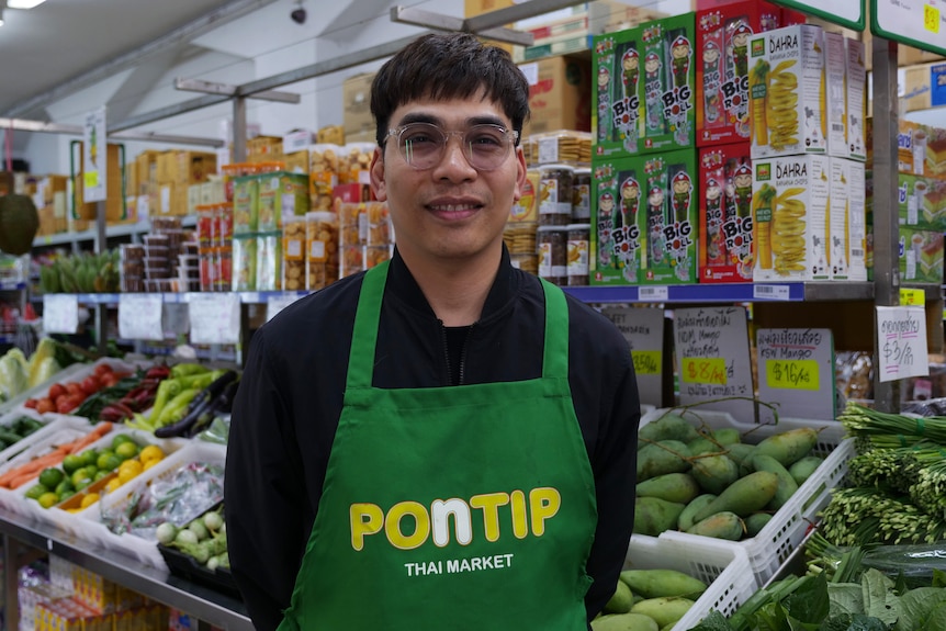 A man smiling standing in front of fresh groceries in a store