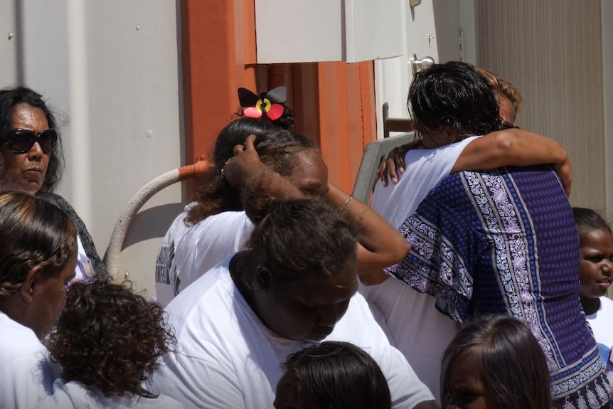 A group of people cuddle outside what appears to be a funeral.