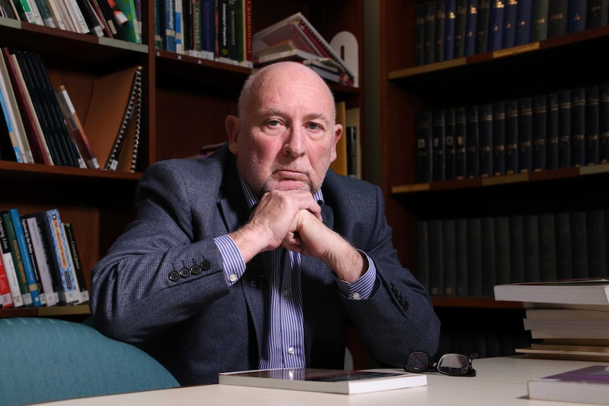 Professor Harry Blagg sits at his desk in his office with rows of books lining the shelves behind him.