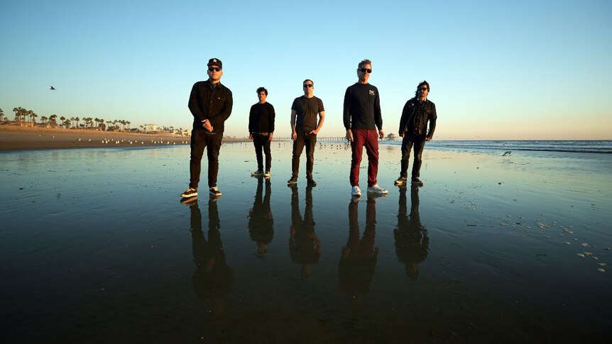 The five members of The Bronx all standing on a beach at dusk