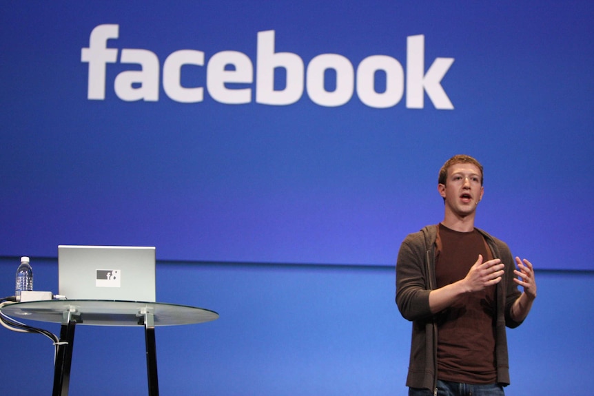 Facebook CEO Mark Zuckerberg talking to an audience with a Facebook sign behind him