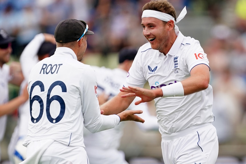 Two cricketers, one in a white headband, look excited as they celebrate a wicket.