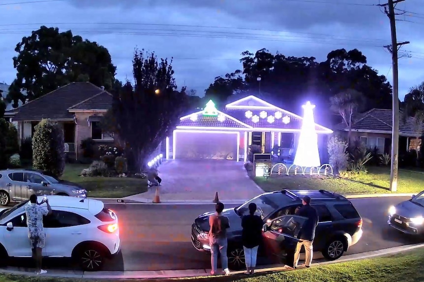 Cars are parked and people stand out the front of Nick Triantafillou's house lit up with Christmas lights.