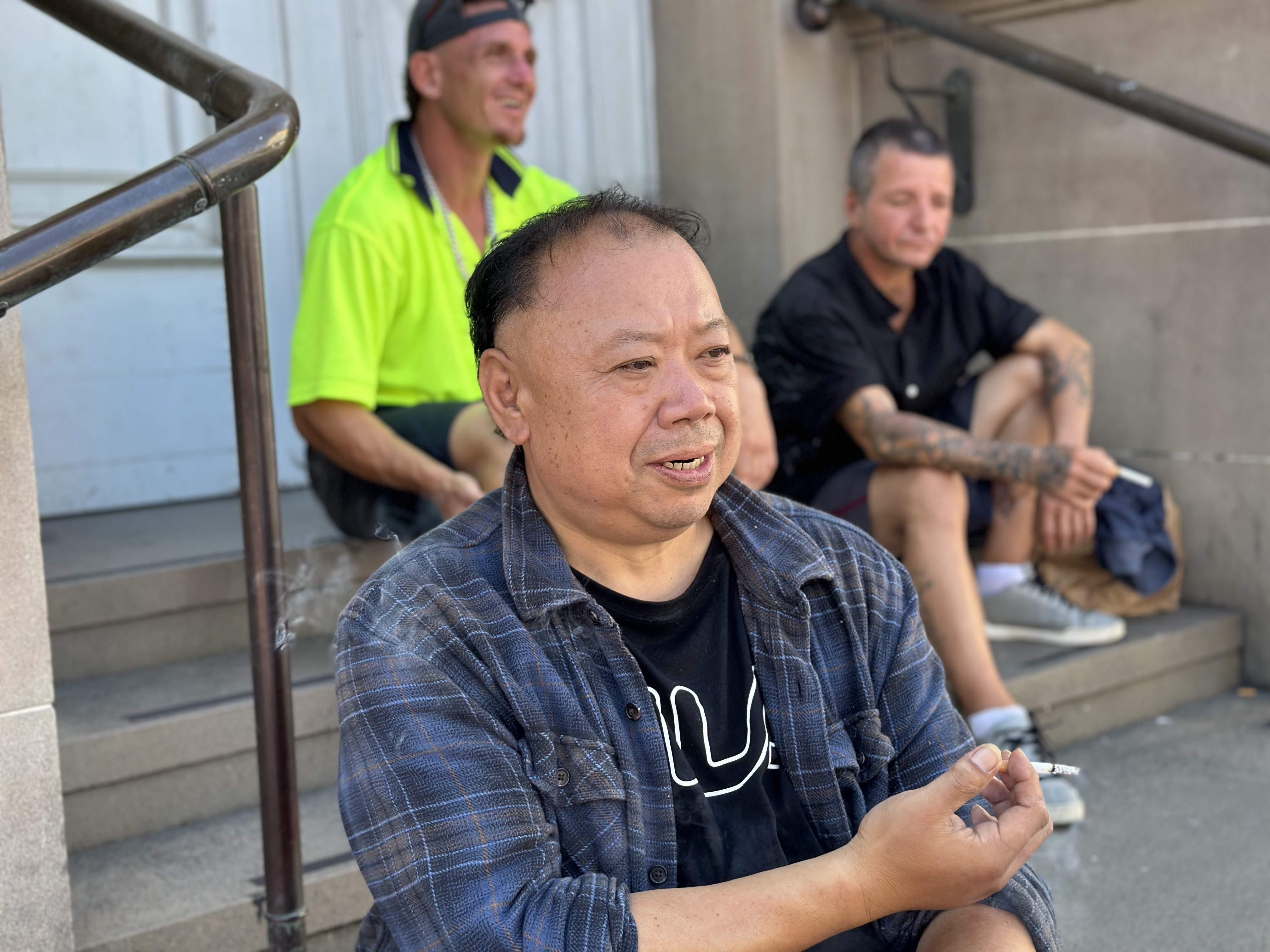 Ronald Liu sits on a step in Western Sydney with a cigarette in hand