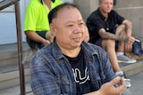 Ronald Liu sits on a step in Western Sydney with a cigarette in hand