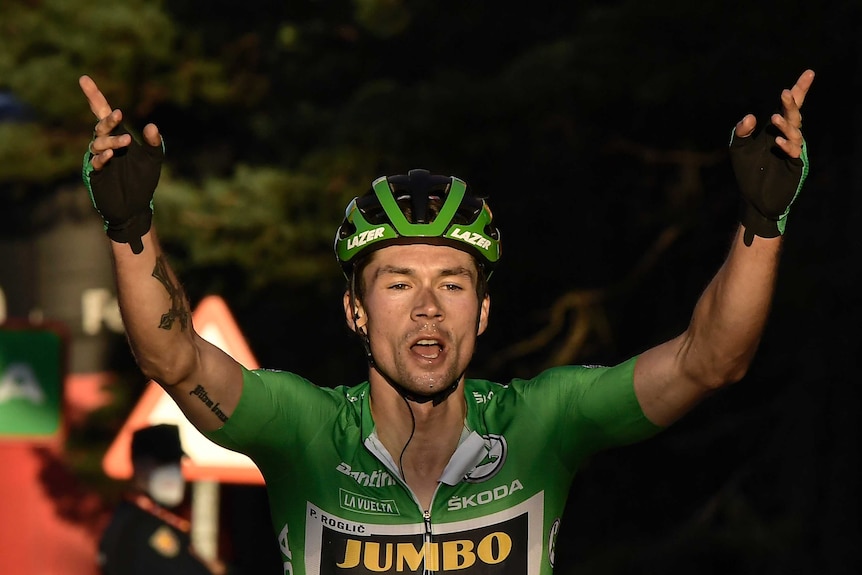 Primoz Roglic celebrates with both hands up in the air, fingers pointing up