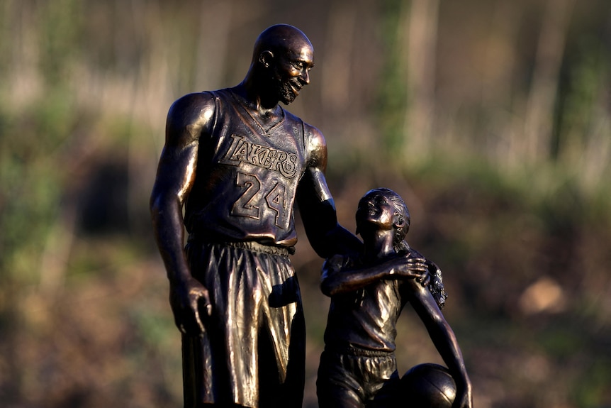 A bronze statue of a man wearing a basketball jersey with his arm around a young girl holding a basketball.