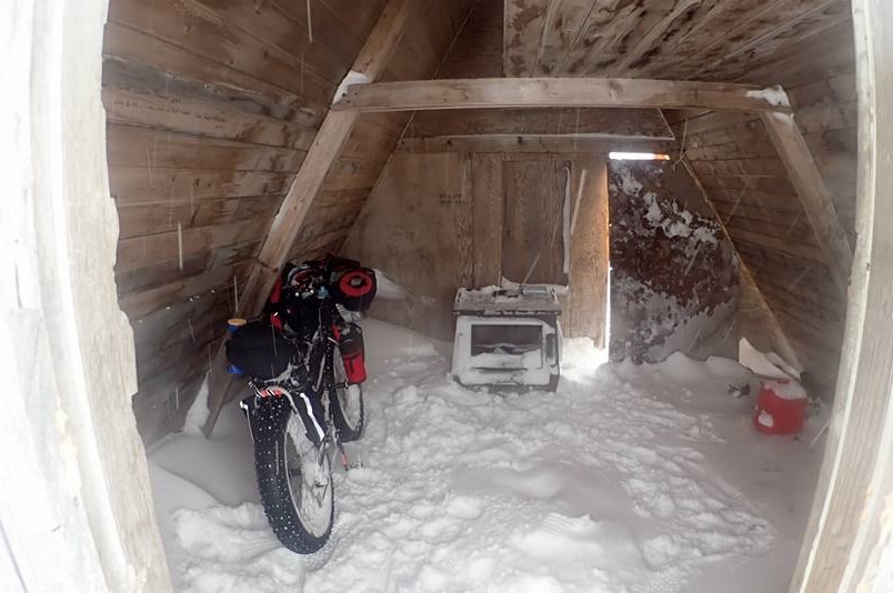 The inside of a snow-filled wood cabin with a bike inside.