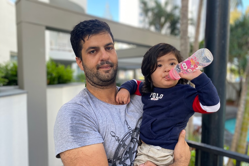 a man holds a toddler, who is drinking from a baby bottle