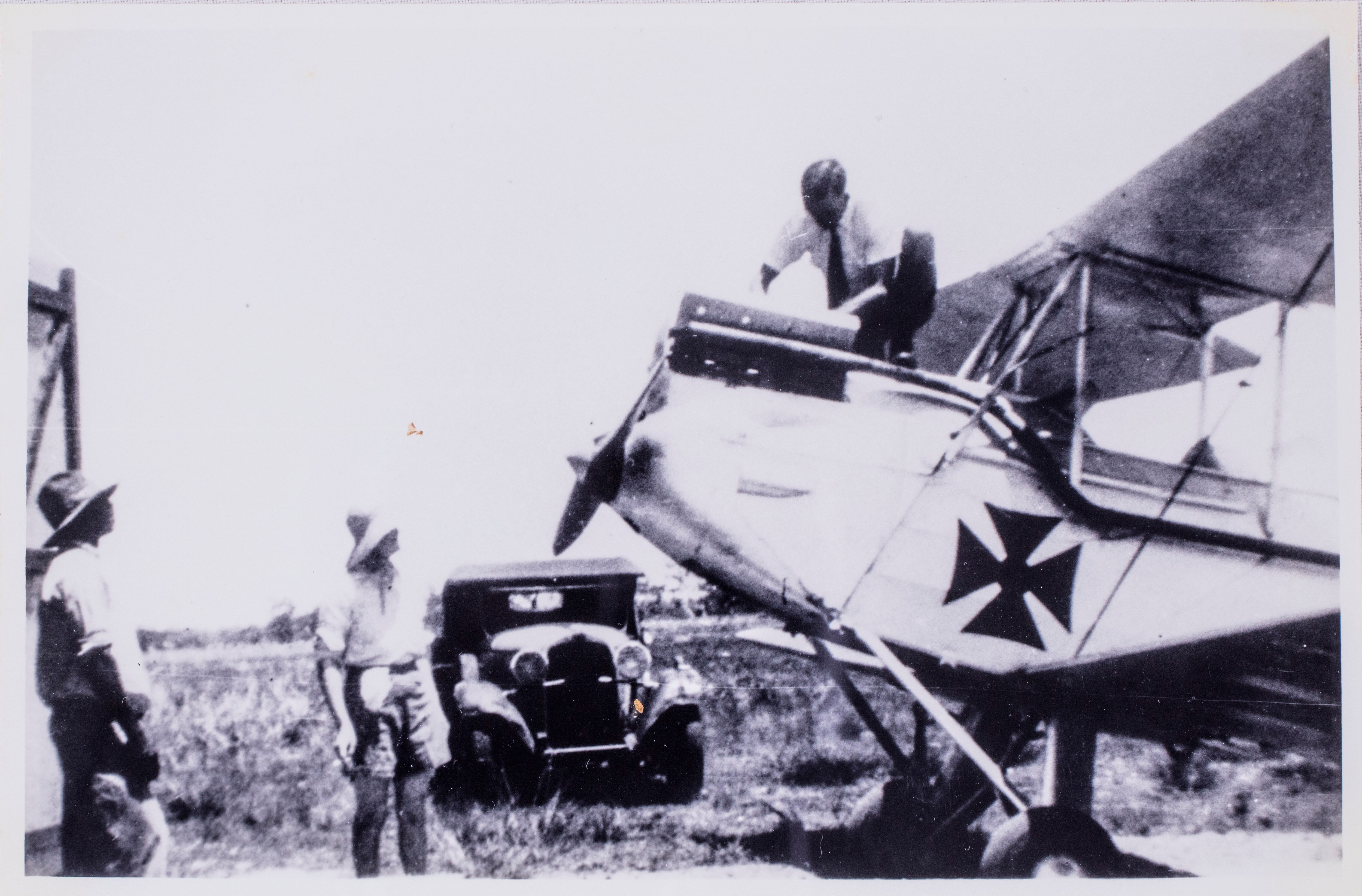 A man stands on top of an old plane while two men look up at him.  The photo is old and in black and white. 