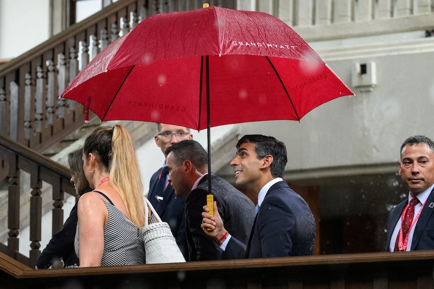 Rishi Sunak holds a big red umbrella 