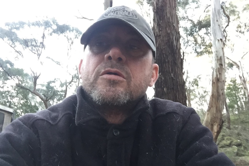 A selfie of a man in the bush wearing a cap and jumper with a beard. 