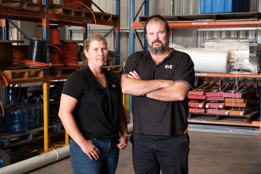 A woman and man wearing black polo shirt standing in the warehouse of their electrical contracting business