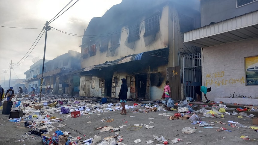 People stand amid debris in front of a burned-out building after days of unrest in Honiara, Solomon Islands.