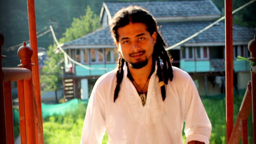Nilotpal Das looks at the camera as he walks up an outdoors staircase. He has dreadlocks and is wearing a white shirt.