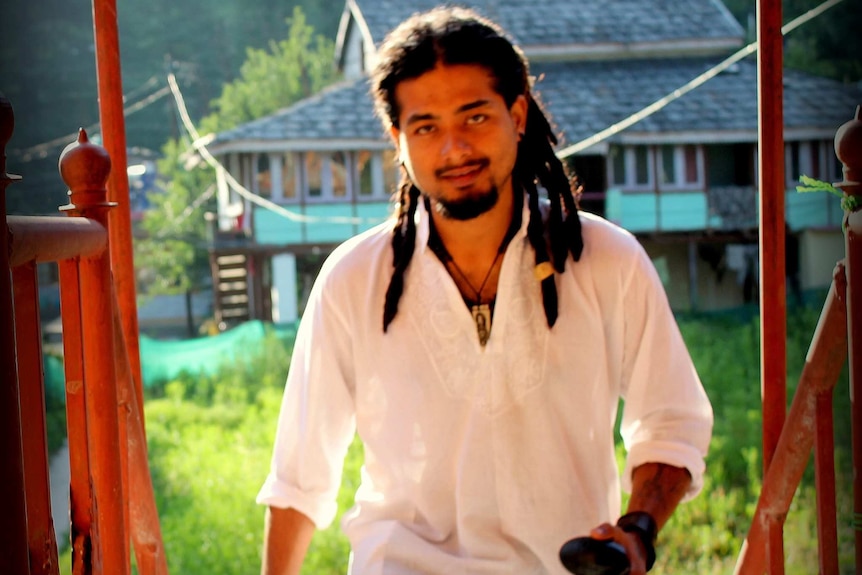 Nilotpal Das looks at the camera as he walks up an outdoors staircase. He has dreadlocks and is wearing a white shirt.