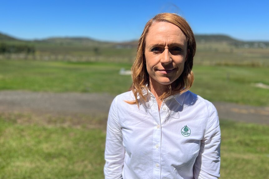 A woman standing in a paddock wearing a professional button up it has a small green logo embroidered on the front