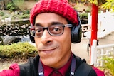 Rahul Gairola wearing a red beanie and headphones in a garden.