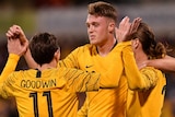 Harry Souter embraces and celebrates with Jackson Irvine and Craig Goodwin after a goal. They all wear yellow Socceroos jumpers