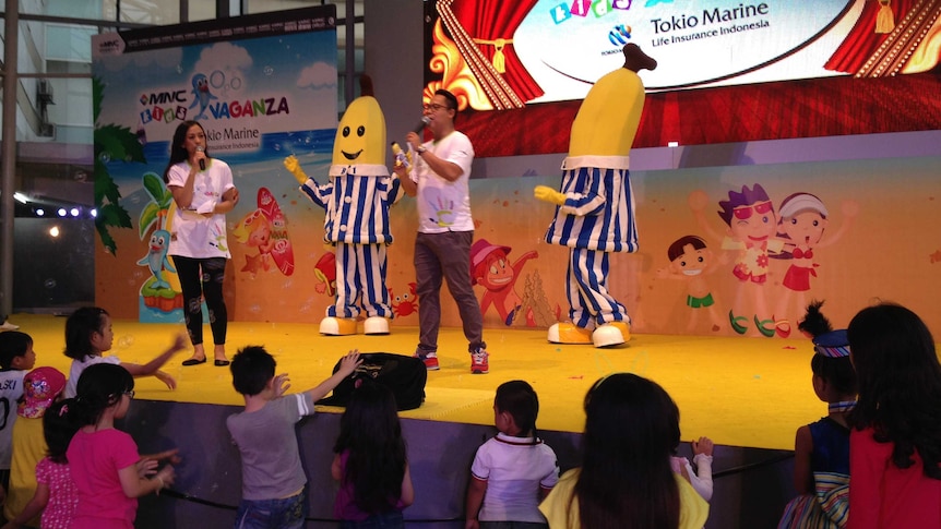 Children gather in front of a stage on which a man and woman address the audience in front of the Bananas in Pyjamas.