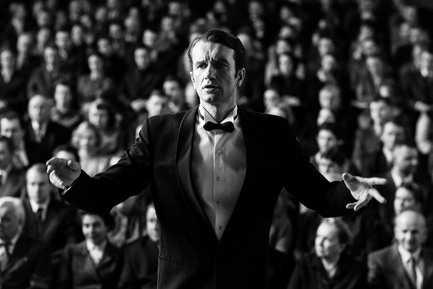 Black and white still of Tomasz Kot as conductor in front of audience in 2018 film Cold War.