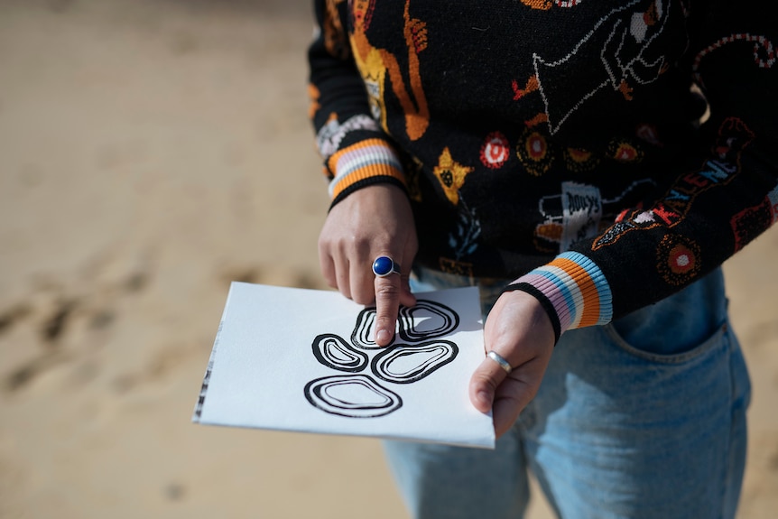 Exterior scene beach an artist points to designs on paper