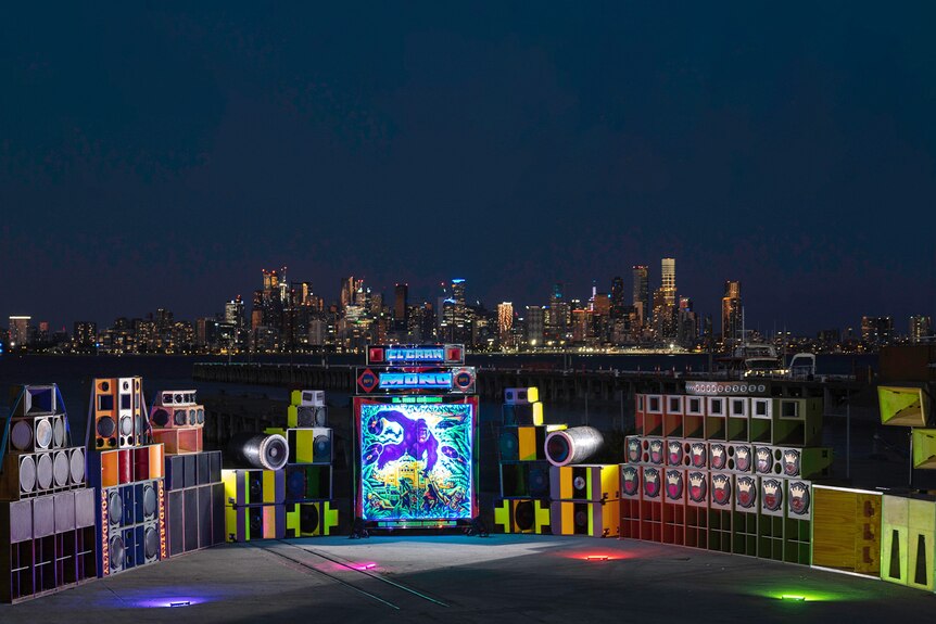 Speaker stacks are arranged in a semi-circle, on either side of a bright image of a gorilla, overlooking the Melbourne skyline