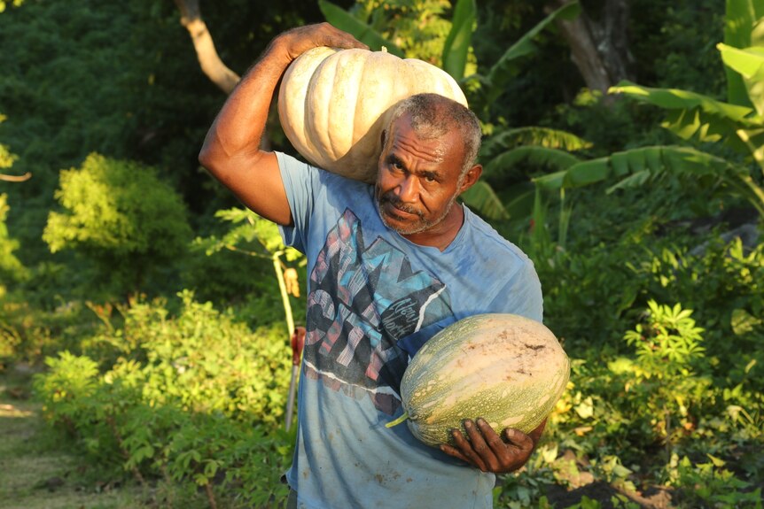 A man holds a melon and pumpkin picked from his garden.
