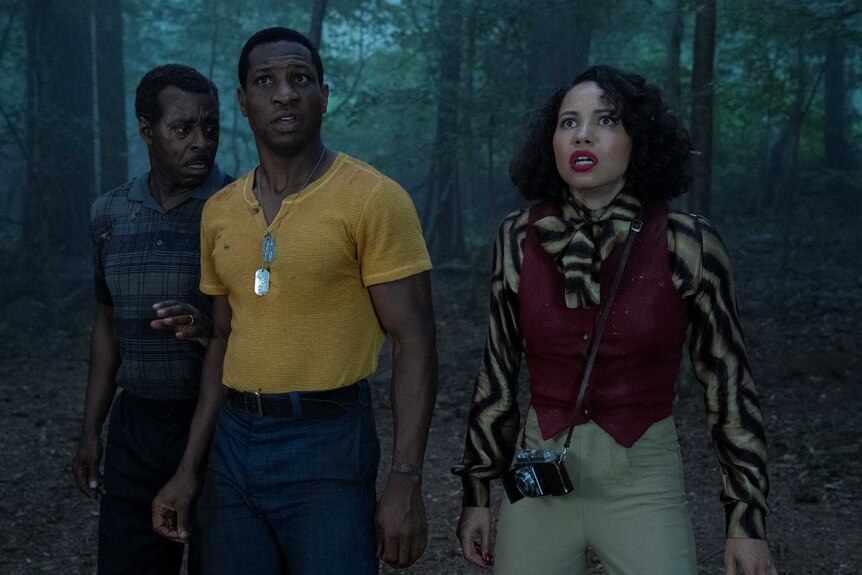 Actors Courtney B. Vance, Jurnee Smollett and Jonathan Majors in a dark forest looing scared in TV show Lovecraft Country