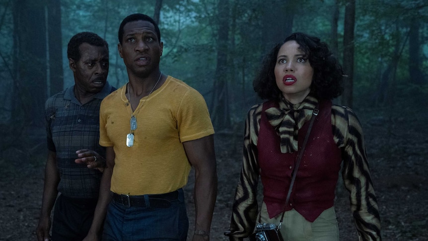 Actors Courtney B. Vance, Jurnee Smollett and Jonathan Majors in a dark forest looing scared in TV show Lovecraft Country