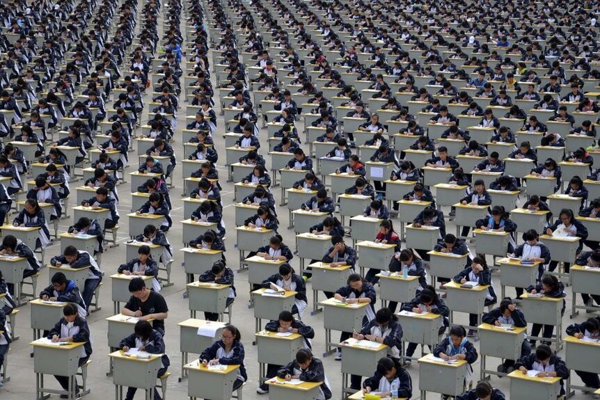 Hundreds of Chinese students in a hall sit at desks taking exams.