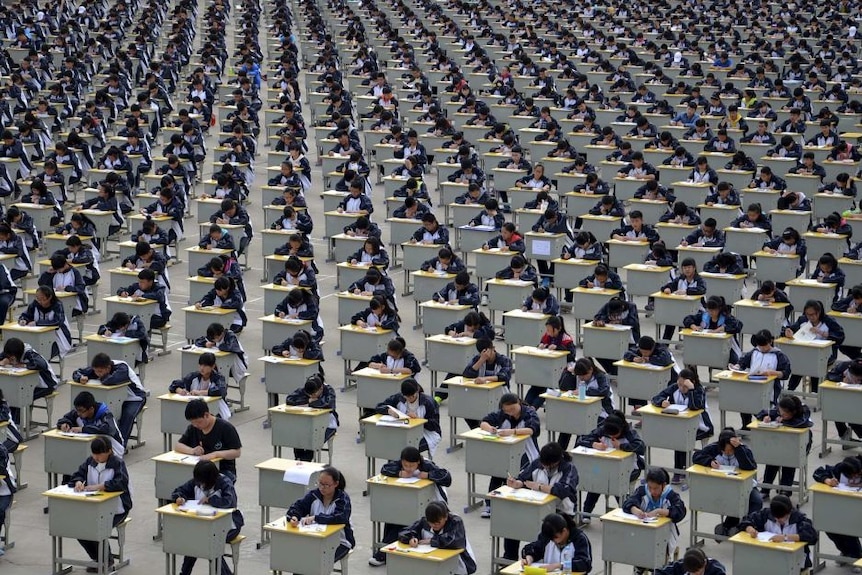 Hundreds of Chinese students in a hall sit at desks taking exams.