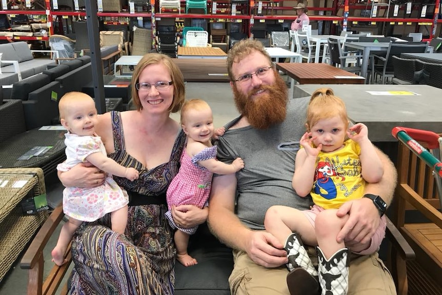 Mum and dad sit with three young children on lap smiling at camera.