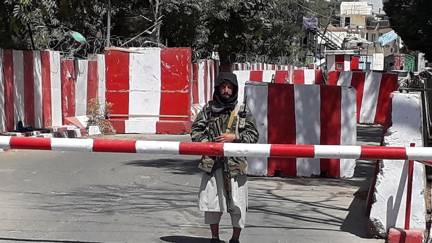 A Taliban soldier stands behind a road barrier.