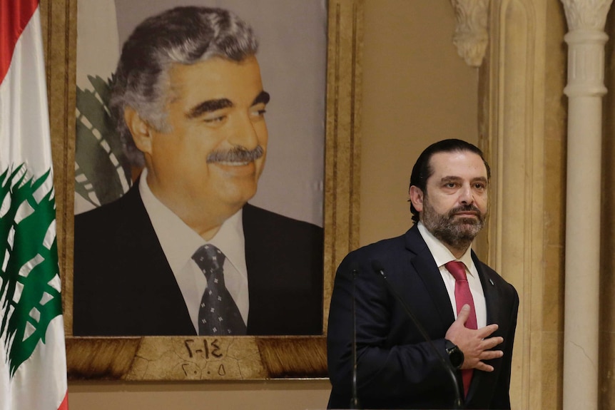 Lebanese Prime Minister Saad Hariri stands near a Lebanese flag holding his hand on his heart.