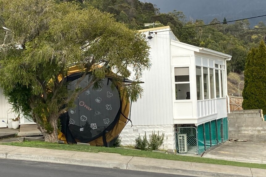 An upended trampoline sits against the side of a house
