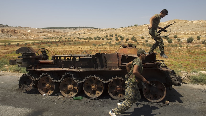 Syrian rebel fighters with a burnt army tank