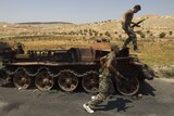 Syrian rebel fighters with a burnt army tank