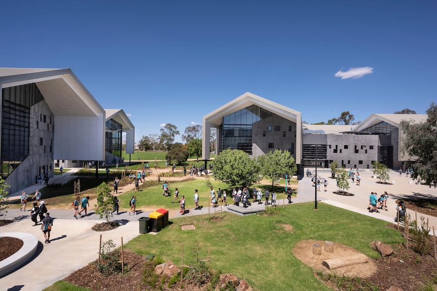 A view of modern school buildings with students in uniforms walking along paths and grass in front of them.