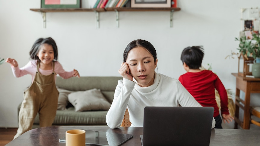 Mum looking burned out while sitting in front of laptop, for a story about dealing with mum shame and guilt.