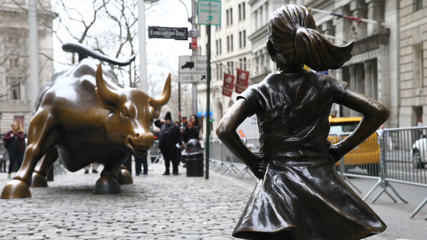 Photograph of statue of Fearless Girl in New York that depicts a small girl standing proudly in front of giant bull