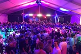 Hundreds of teenagers in a marquee dancing with disco lights and a DJ at a podium.