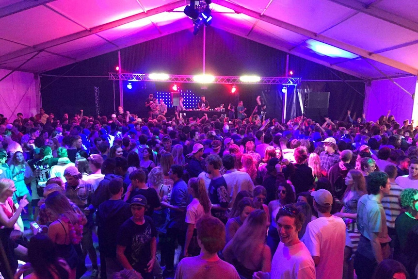Hundreds of teenagers in a marquee dancing with disco lights and a DJ at a podium.