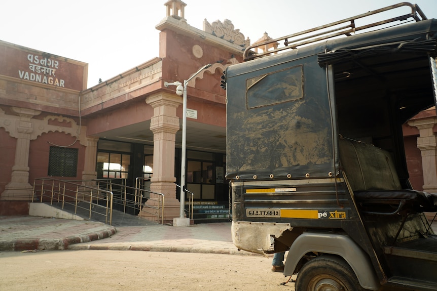 A green truck parked outside a pink brick building with ornate columns at the front